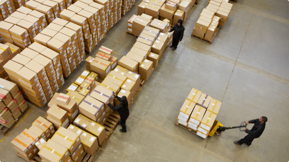 Birds eye view of a male moving a pallet of boxes in a full warehouse