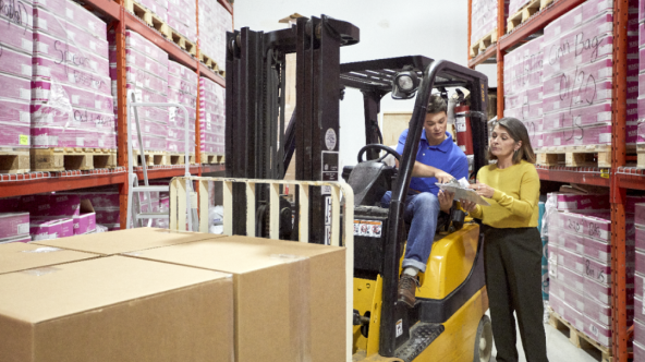 Female and male on a forklift looking at a clipboard in a warehouse