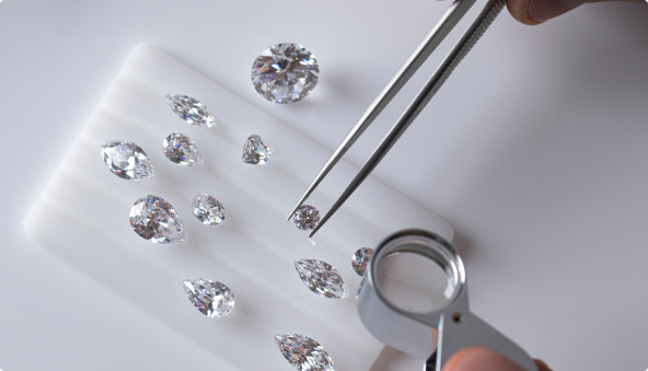 Tweezers picking up a diamond from a tray holding multiple different sized diamonds