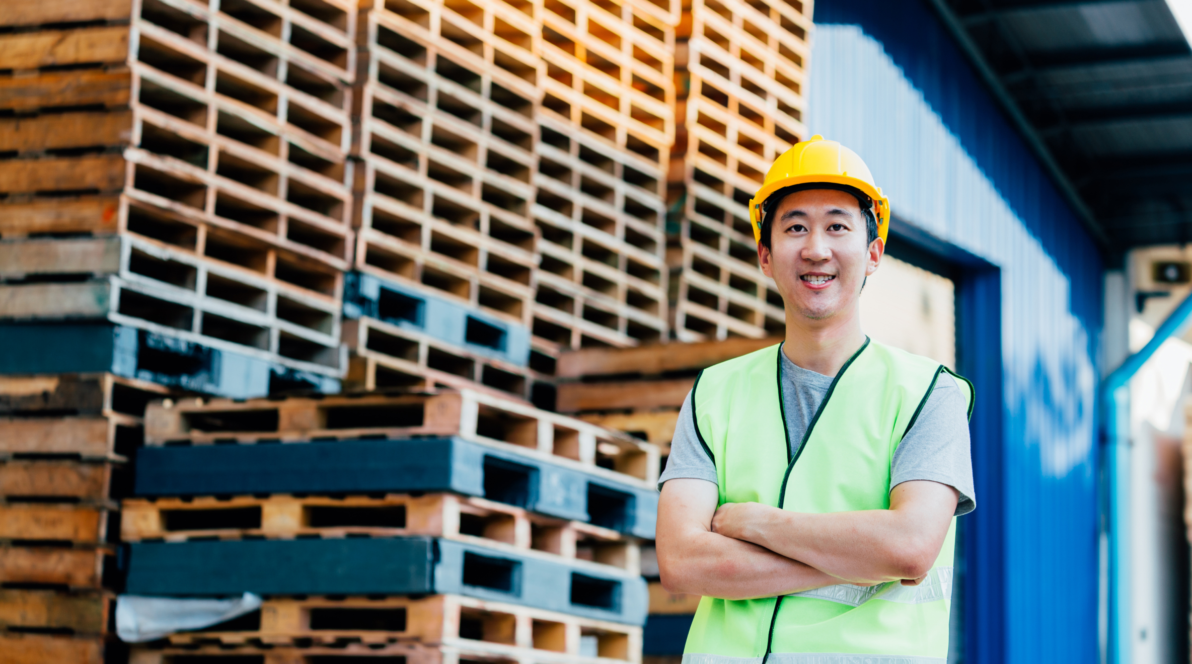  Male wearing a hard hat and vest standing in front of pallets with arms folded