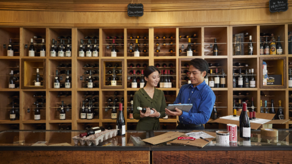 Male showing a tablet to a female holding a bottle in a wine shop
